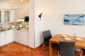 Eine kompakte Küche mit weißen Schränken, einem Esstisch für vier Personen und einem Bild an der Wand.