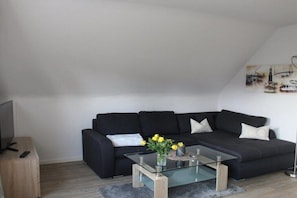 Ein modernes Wohnzimmer mit einem schwarzen Sofa, einem Glastisch und einem Fernseher auf einem Holzboden.
