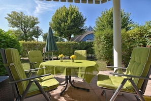 Ein runder Tisch mit grüner Tischdecke, umgeben von vier grünen Stühlen, draußen mit Blick auf einen Garten.