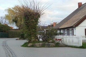 Ein weißes Gebäude mit einem Reetdach, einem weißen Zaun und einer gepflasterten Auffahrt.