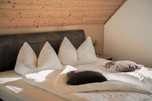 Ein Schlafzimmer mit schrägen Wänden, einem Bett mit weiß gestreiften Kissen und einem Nachttisch mit einer Lampe.