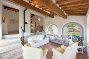 A spacious living area with a white sofa, striped armchairs, a stone fireplace, and a view through arched windows. - Your Authentic Chianti Escape in San Sano (San Sano)