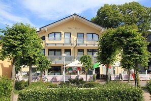 Ein zweistöckiges Gebäude mit Balkonen, einem Schild mit der Aufschrift 'Villa Wauji' und Sitzgelegenheiten im Freien.