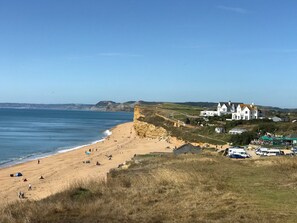 Ein Küstenstrand mit einem Gebäude an der Klippe, einem Sandstrand und blauem, wolkenlosem Himmel.