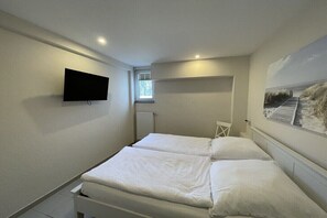 Ein Schlafzimmer mit zwei Betten, einem Fernseher, einem Fenster und einem Bild an der Wand.