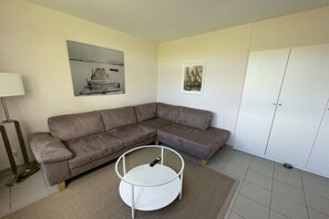 Ein Wohnzimmer mit einem Ecksofa, einem runden Couchtisch und zwei an der Wand befestigten Bildern.
