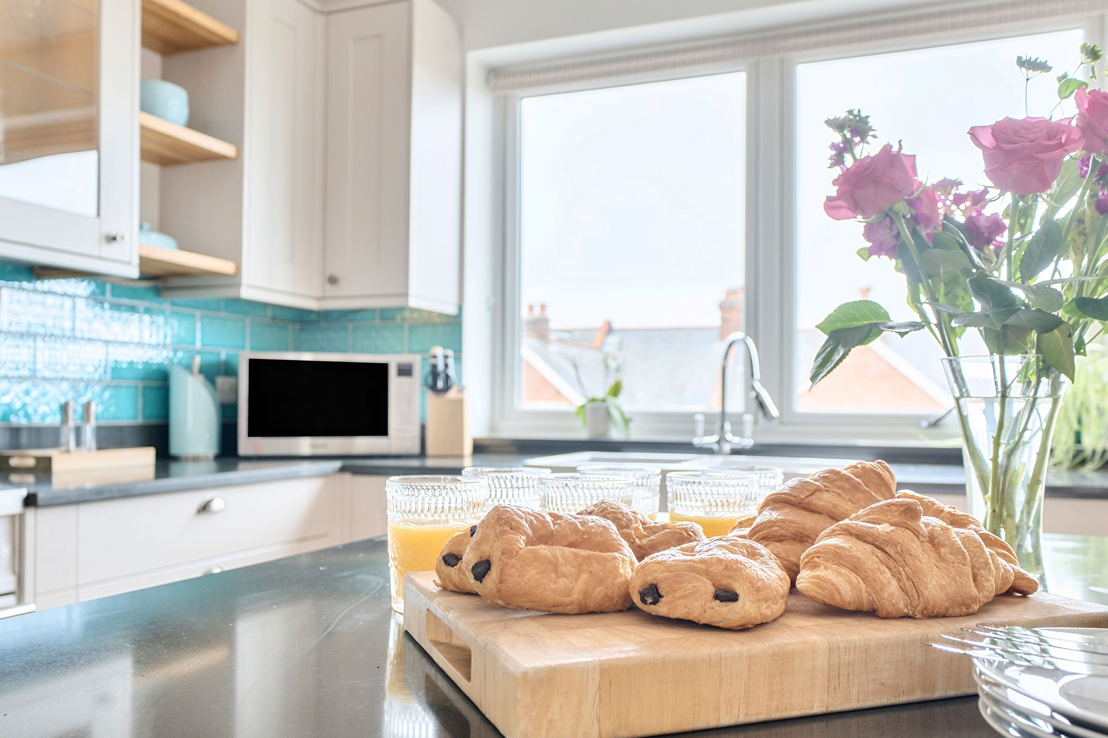 Een keuken met een houten snijplank, croissants en glazen sinaasappelsap.