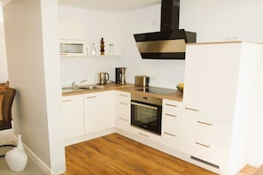 Eine moderne Küche mit weißen Schränken, einer Edelstahl-Dunstabzugshaube, einem Einbauofen und einer Holz Arbeitsplatte.