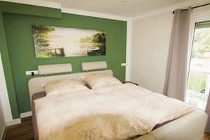 Ein Bett mit Kopfteil, ein Gemälde darüber und ein Fenster mit Vorhängen.