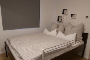 A single bed with a white and black checkered bedspread, a headboard, and a window with a blind. - Ecki's holiday home "Komm An de Bäk" (Alt Schönau)