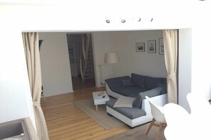 Ein modernes Wohnzimmer mit Sofa, einem kleinen Beistelltisch, einer Lampe und einem Sessel.
