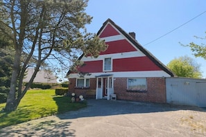 Ein rotes und weißes Haus mit Garage, Rasen und Baum.
