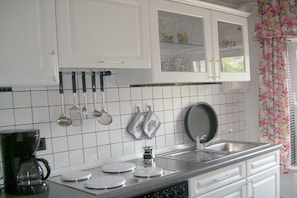 A kitchen with white cabinets, a tiled backsplash, a coffee maker, a frying pan, and hanging utensils. - Holiday apartment with 1 bedroom (Neustrelitz O.T. Klein Trebbow)
