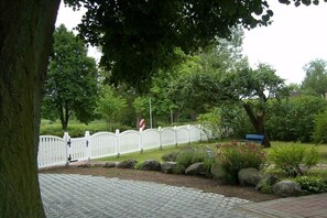 A paved pathway leading to a white picket fence, a bench, and a tree-lined area. - Holiday apartment with 1 bedroom (Neustrelitz O.T. Klein Trebbow)