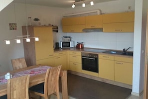 A compact kitchen with yellow cabinets, a microwave, a stove, and a sink. - Holiday apartment with 2 bedrooms (Kühlungsborn)