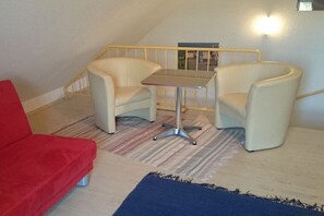 A room with a red sofa, two armchairs, a small table, a striped rug, and a staircase. - Holiday apartment with 2 bedrooms (Kühlungsborn)