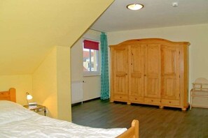 A bedroom with a bed, a wooden wardrobe, a nightstand with a lamp, and a window with a curtain. - Holiday apartment with 2 bedrooms (Kühlungsborn)