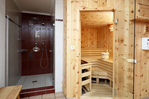 A wooden sauna with a glass door, a shower area with a glass enclosure, and a wooden bench. - Holiday apartment in Patergassen with sauna (Patergassen)