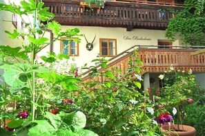 Ein traditionelles Gebäude mit Balkon, Treppe und einem Garten mit verschiedenen Pflanzen und Blumen.