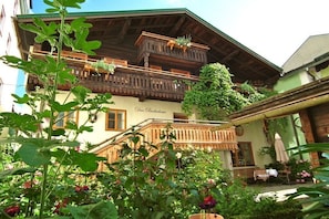 Ein traditionelles Holzhaus mit Balkonen und einem Blumengarten, mit einem Schild, auf dem 'Das Baderhaus' steht.