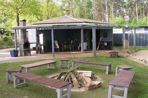 Un espacio al aire libre cubierto con bancos, una chimenea y un edificio con techo a dos aguas.