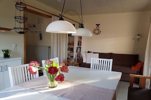 Ein Essbereich mit einem weißen Tisch, Stühlen, einer Blumenvase und Pendelleuchten.