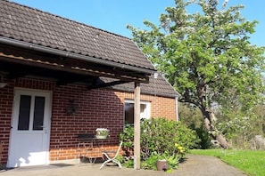 Ein Backsteinhaus mit Ziegeldach, einer weißen Tür und einer kleinen Veranda.
