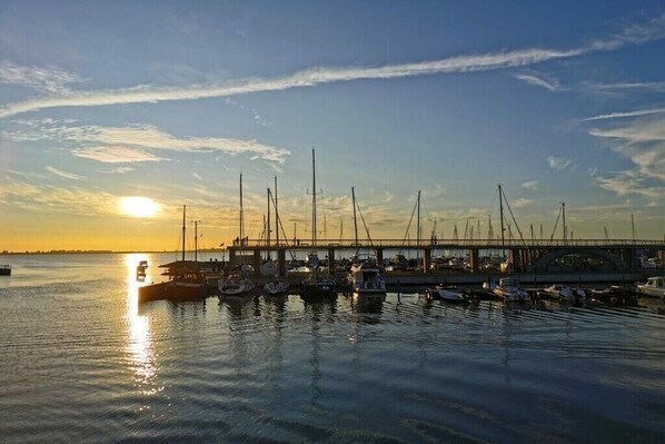 A marina with boats docked, a bridge in the background, and the sun setting over the water. - Holiday home in Wiek with swimming pool (Wiek)