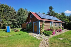A wooden cabin with a solar panel roof, a stone pathway, and a garden with pink flowers. - Holiday home in Wiek with swimming pool (Wiek)