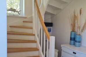 A staircase with wooden steps and white railings, a white dresser with two blue vases, and a window with a model airplane. - Holiday home with 2 bedrooms (Oldenburg in Holstein)