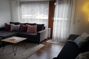 Ein Wohnzimmer mit einer Couch, einem Couchtisch und einem Fenster mit durchsichtigen Vorhängen.