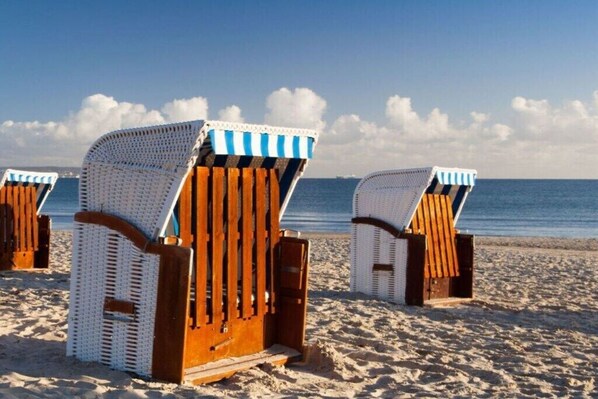 Beach chairs with a striped top and wooden base on a sandy beach with the ocean in the background. - Country house at Goor (Vilmnitz)