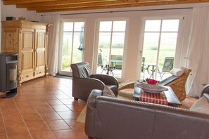 A living room with a fireplace, leather sofas, a dining table with a red flower, and large windows with a view of the outdoors. - Country house at Goor (Vilmnitz)
