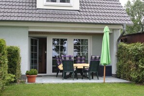 A house with a covered patio, a table with chairs, and a green umbrella. - Holiday home with 1 bedroom (Trassenheide)