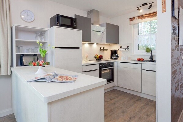 A modern kitchen with white cabinetry, a built-in oven, and a microwave. - Holiday home with 1 bedroom (Trassenheide)