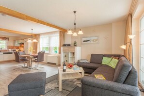 A modern living room with a sofa, a coffee table, and a dining area with chairs. - Holiday home with 1 bedroom (Trassenheide)