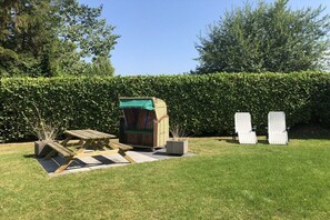 A picnic area with a wooden table and chairs, a covered seating area, and a hedge in the background. - "Lübeck Bay" in the TINTIN House (Scharbeutz)