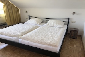 A double bed with white bedding, a wooden floor, and a window with curtains. - "Lübeck Bay" in the TINTIN House (Scharbeutz)