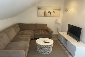 A modern living room with a sectional sofa, a round coffee table, a flat-screen TV, and a painting on the wall. - "Lübeck Bay" in the TINTIN House (Scharbeutz)