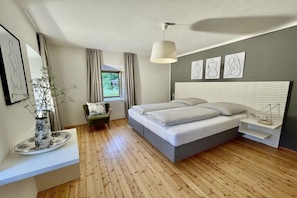 A modern bedroom with a bed, bedside tables, a chair, a window, and artwork on the wall. - Holiday apartment with 2 bedrooms (Amlach bei Greifenburg)