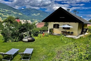 A house with a sloped roof, a small patio with a table and chairs, and a grassy yard with two solar-powered lounge chairs. - Holiday apartment with 2 bedrooms (Amlach bei Greifenburg)