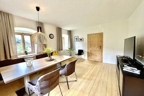 A dining area with a wooden table, chairs, a hanging light fixture, and a television on a stand. - Holiday apartment with 2 bedrooms (Amlach bei Greifenburg)