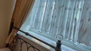 Un dormitorio con una cama, una ventana con cortinas translúcidas y un cabecero de metal.