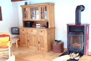 Ein Holzschrank mit Glastüren, ein Fernseher, ein roter Kaminofen und ein Korbwäscher auf dem Boden.