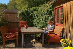 Ein Holztisch mit Stühlen, ein Hund und eine Person beim Lesen.