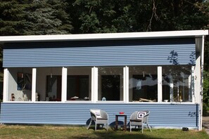 Un bâtiment moderne doté d’un toit plat, de grandes fenêtres et d’un porche couvert avec deux chaises et une petite table.