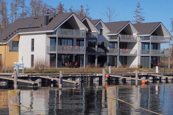 A multi-story building with balconies, a dock, and a calm water body in front. - Apartment in Plau am See with swimming pool (Plau am See)