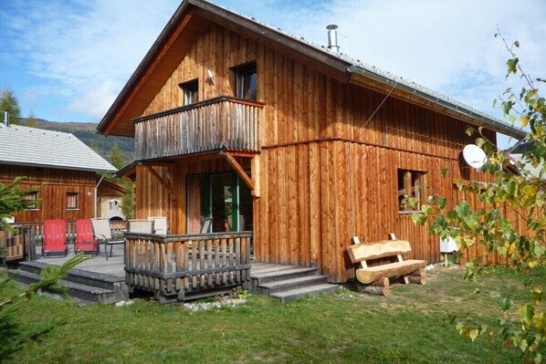 A wooden cabin with a balcony, a porch, and a small outdoor seating area.