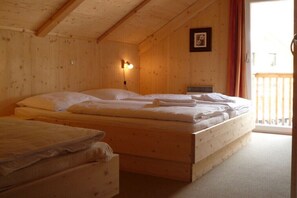 A wooden cabin room with a bed, a smaller bed or couch, a wall-mounted light, and a balcony.