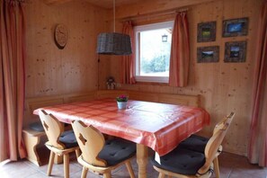 A wooden dining room with a table and chairs, a window with curtains, and wall-mounted pictures. - Cabin with 1 bedroom (Stadl an der Mur)